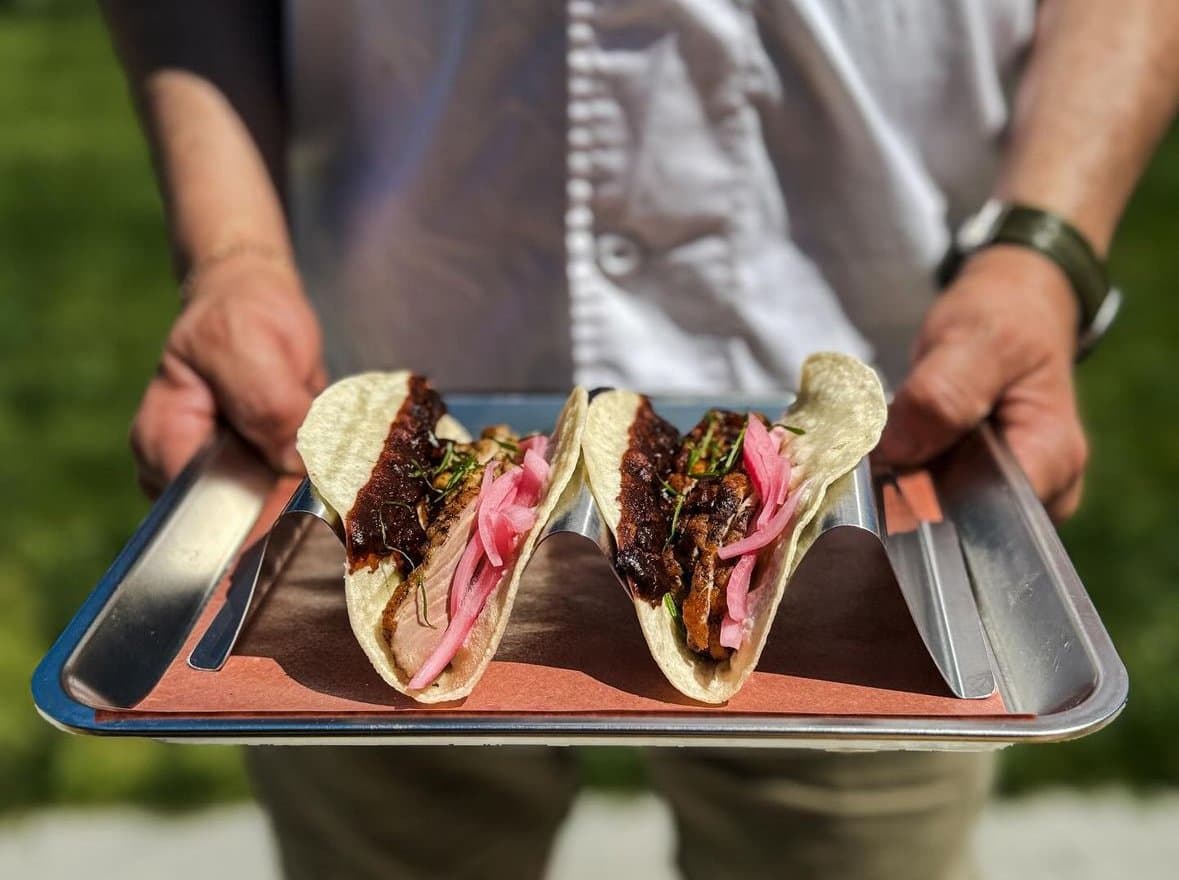 Two tacos with pickled onion on a metal tray, carried out to a customer
