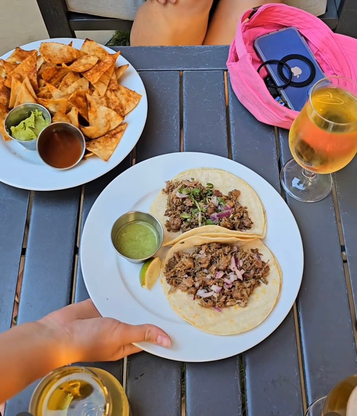 An outdoor table set with tacos, tortilla chips, guacamole and drinks